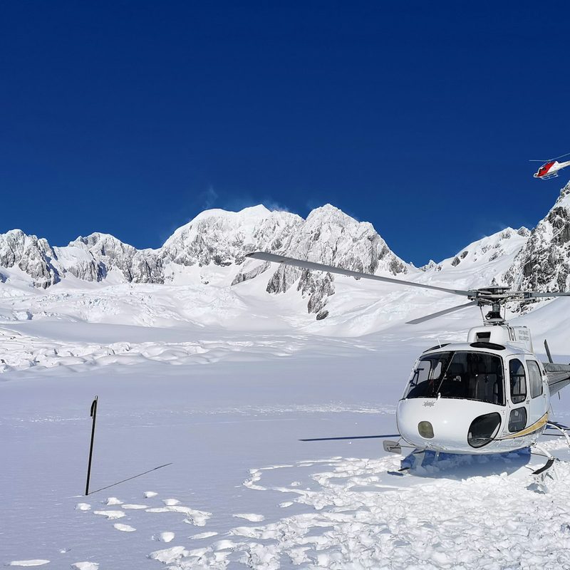 Helicopter landed on a glacier below snow peaks